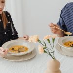 Two women enjoying homemade pumpkin soup at a dining table with floral decor.