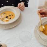 A top view of two people enjoying creamy pumpkin soup with elegant table setting.